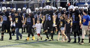Football team captains hold the hands of children with cancer as they walk out to midfield for the coin toss.