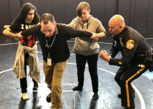 Caption: Social Studies teacher Sean Burke is held by two students as School Resource Officer Bob Lee instructs them during volunteer training at Quakertown Community High School. 