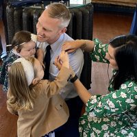 Holding daughter Zelie, Lucas Brommer is all smiles as his wife Madison and daughter Millie help him with his new Lieutenant Colonel pins.